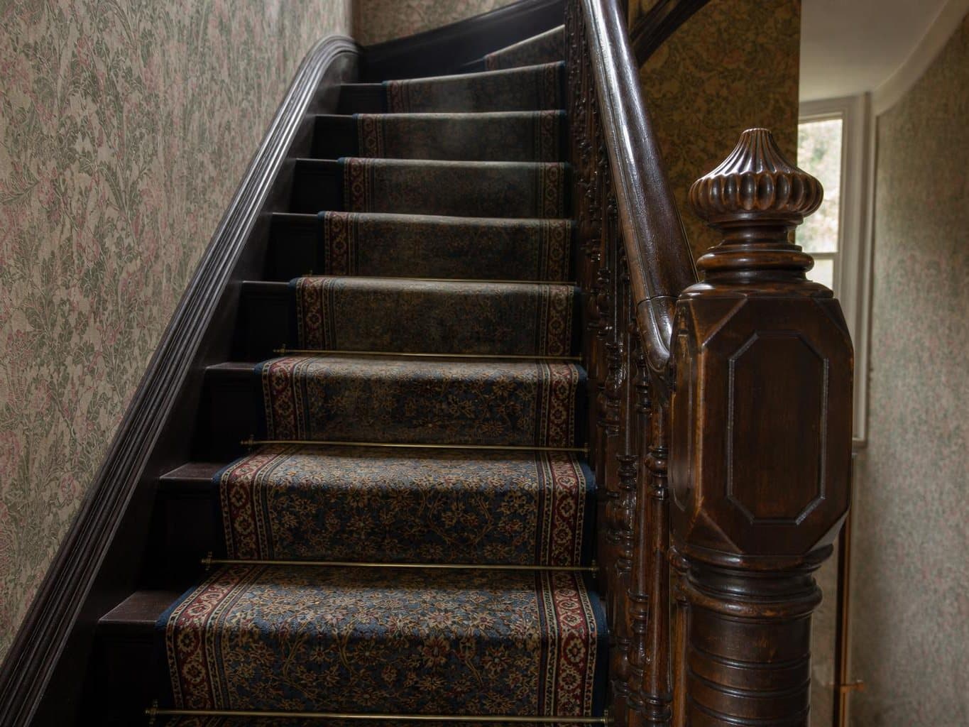 Narrow Victorian staircase with a carpet runner held by stair rods, the lower treads cleaned and bright