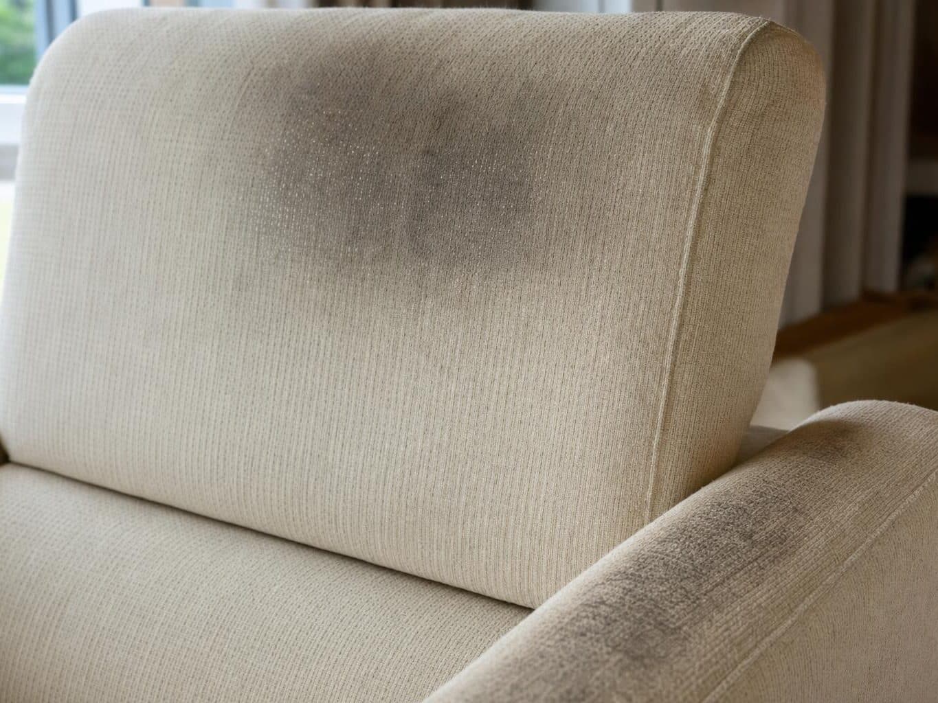 Headrest and arm of a cream sofa showing darkened body-oil soiling against clean fabric